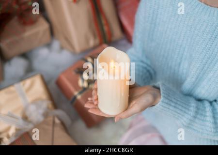 Frau in hellblauem Pullover mit dicker weißer Wachskerze in den Händen. Weihnachtsfeiertage. Weibliche Hände mit Wachskerze. Platz kopieren, Nahaufnahme Stockfoto