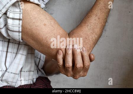 Schmerzen im Ellenbogengelenk des südostasiatischen älteren Mannes. Konzept von Ellenbogenschmerzen, rheumatoider Arthritis und Armproblemen. Stockfoto