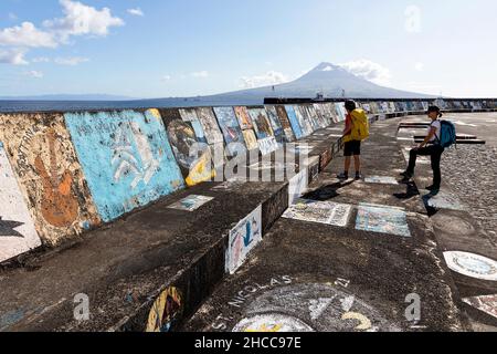 Mutter und Sohn mit einem Rucksack und Blick auf die bemalte Hafenwand mit Graffiti mit dem Berg Pico im Hintergrund, Horta, Insel Faial, Azoren, Portugal Stockfoto