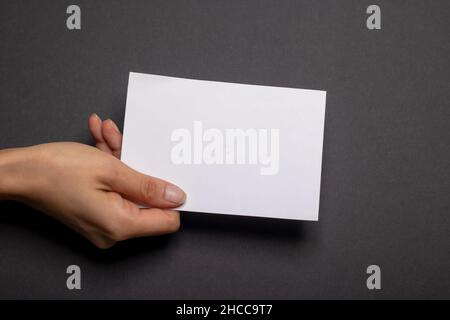 Weibliche Hand hält ein leeres Stück Papier mit Kopierraum vor einem schwarzen Hintergrund Karton Stockfoto