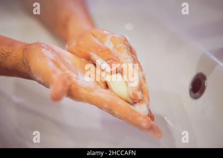 Ein Mann wäscht seine Hände vorsichtig mit weißer Seife über einem weißen Keramikwaschbecken im Badezimmer. Sauberkeit und Hygiene. Stockfoto