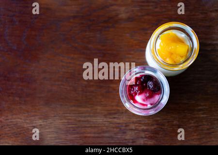 Griechischer Joghurt mit Beeren und Mango in Gläsern auf Holzboden Stockfoto