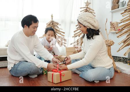 Neugieriger Junge, der seine Eltern zu Hause beim Verpacken und Dekorieren von Weihnachtsgeschenken ansieht Stockfoto