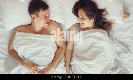 Das junge Paar kommuniziert nach dem Aufwachen im Bett liegend Stockfoto