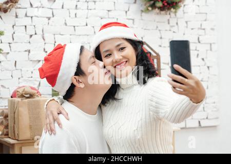Mann in santa hat küssen Frau auf der Wange, wenn sie Selfie auf SM, artphone nimmt Stockfoto