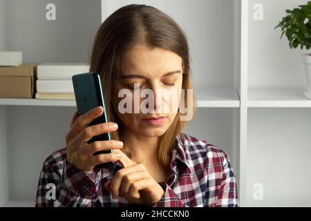 Eine blinde Frau nutzt ein Mobiltelefon, während sie den Ton hört, indem sie auf den Bildschirm klickt. Das Konzept von Menschen mit Sehbehinderung. Stockfoto