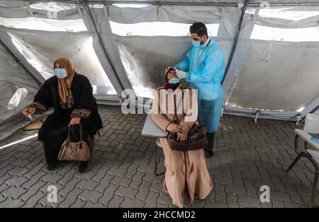 Gaza, Palästina. 27th Dez 2021. Palästinensische Gesundheitshelferin sammelt während eines COVID-19-Massentests eine Abstrichprobe von einer Frau für COVID-19-Tests.das palästinensische Gesundheitsministerium im Gazastreifen hat den ersten Fall der omicron-Variante in Gaza angekündigt und sagte, dass diese Infektion durch Israel in den Gazastreifen übertragen wurde Ein palästinensischer Arbeiter, der in Israel arbeitete, forderte die Menschen auch auf, eine frühzeitige Untersuchung durchzuführen, indem Proben entnommen und die notwendigen Impfungen gegen die COVID-19-Pandemie erhalten wurden. Kredit: SOPA Images Limited/Alamy Live Nachrichten Stockfoto