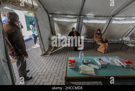 Gaza, Palästina. 27th Dez 2021. Die Palästinenser warten auf einen Coronavirus-Test vor einem Zelt der medizinischen Klinik im Al-Shati-Flüchtlingslager, das palästinensische Gesundheitsministerium im Gazastreifen hat den ersten Fall einer omicron-Variante im Gazastreifen angekündigt und sagte, dass diese Infektion von Israel in den Gazastreifen durch einen palästinensischen Arbeiter übertragen wurde, der in Israel arbeitete, Außerdem baten sie die Menschen, eine frühzeitige Untersuchung durchzuführen, indem sie Proben entnahmen und die erforderlichen Impfungen gegen die COVID-19-Pandemie erhielten. Kredit: SOPA Images Limited/Alamy Live Nachrichten Stockfoto