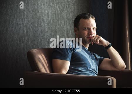 Innen-Porträt eines glücklichen jungen erwachsenen kaukasischen Mannes, der auf einem Sofa sitzt Stockfoto