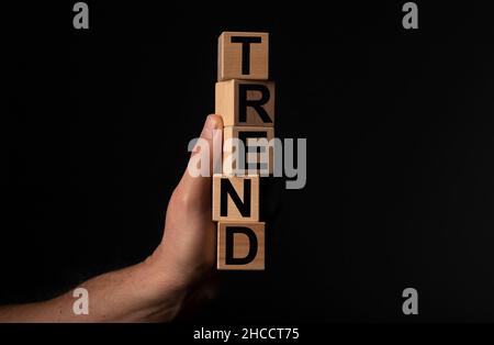 Worttrend auf Holzdices in der Hand über schwarzem Hintergrund. Stockfoto