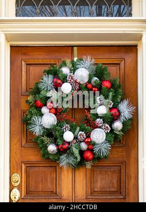 Vordertür mit Weihnachtskranz, aus Kiefernästen, Kiefernzapfen und roter Schleife. Stockfoto