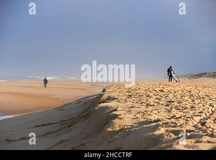 Landschaft eines großen Strandes mit nicht erkennbaren Surfern, die auf den Moment warten, um ins Meer zu kommen und Wellen zu fangen, währenddessen schauen sie sich Fotos auf Th an Stockfoto