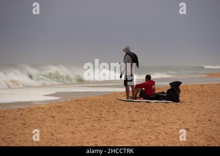 Landschaft eines großen Strandes mit nicht erkennbaren Surfern, die auf den Moment warten, um ins Meer zu kommen und Wellen zu fangen, währenddessen schauen sie sich Fotos auf Th an Stockfoto