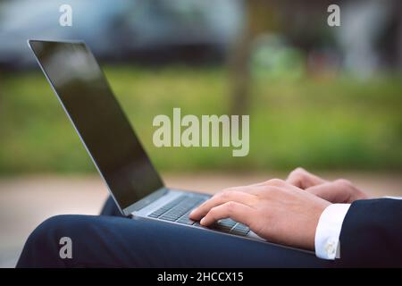 Mann, der im Freien an seinem Laptop arbeitet. Business man Hände tippen auf Computer. Stockfoto