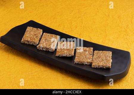 Traditionelle Süßigkeiten Mithai aus Indien isoliert auf gelbem Hintergrund für Makar Sankranti Lohri Gajak auch bekannt als Gur Gajjak Gazak Kachak Til Patti Stockfoto