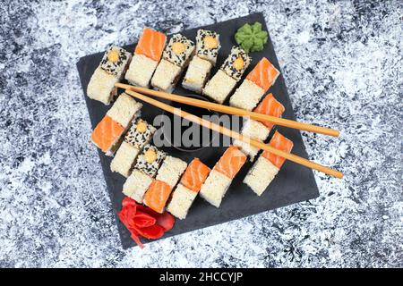 Sushi-Set auf schwarzem Steinteller. Japanisches Sushi-Essen. Brötchen mit Thunfisch, Lachs, Garnelen, Krabben und Avocado. Draufsicht Stockfoto
