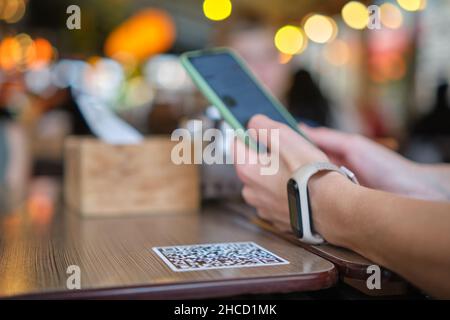 Nahaufnahme der Gäste, die eine Mahlzeit im Restaurant bestellen, während der QR-Code mit dem Mobiltelefon gescannt wird, um ein Online-Menü zu erhalten. Stockfoto