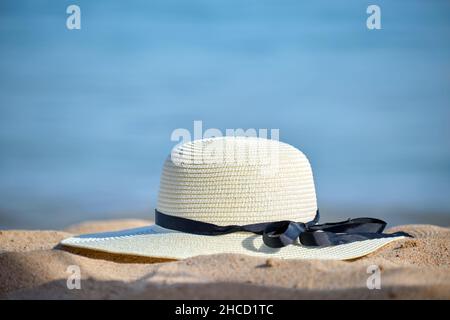 Nahaufnahme von gelbem Strohhut am Sandstrand an der tropischen Küste an warmen, sonnigen Tagen. Konzept für Sommerferien. Stockfoto