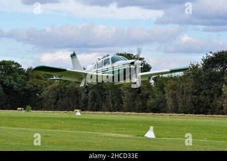 Piper PA-28R-180 Cherokee Arrow Leichtflugzeug G-AWAZ landet auf dem Elmsett Airfield, Suffolk, Großbritannien. Ländliche, von Bäumen gesäumte Graslandepiste. Finale zu landen Stockfoto