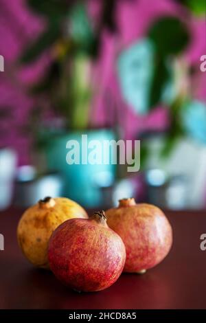 Stillleben mit drei roten Beerengranatäpfeln und Pflanzen, die sich im Hintergrund in der Sonne sonnen Stockfoto