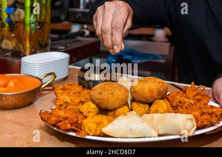 Küchenchefs würzen ein Tablett mit verschiedenen Hindu-Vorspeisen in einem Restaurant Stockfoto