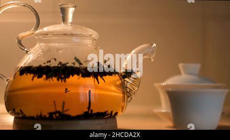 Nahaufnahme der vollen Teekannen und einer weißen kleinen chinesischen Tasse isoliert auf beige Wand Hintergrund. Köstlicher Tee in einer Glas-Teekane in der Nähe von traditionellen Gaiwan und ein Stockfoto