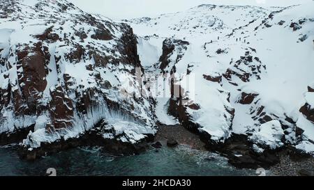 Luftaufnahme von steilen Felsen mit weißem Schnee durch das blaue Meer bedeckt, Schönheit der Winter Natur Konzept. Flug über die wunderschöne felsige Küste in der Wintersaison. Stockfoto