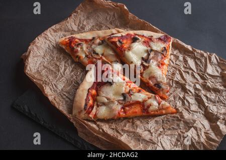 Scheiben frisch gebackene Pizza auf einer schwarzen Tafel auf dunklem Hintergrund Stockfoto