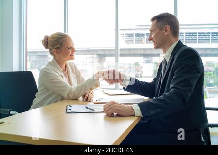 Glückliche junge Geschäftsfrauen und Geschäftsleute, die im modernen Büro zusammenarbeiten, schütteln die Hände und lächeln Stockfoto