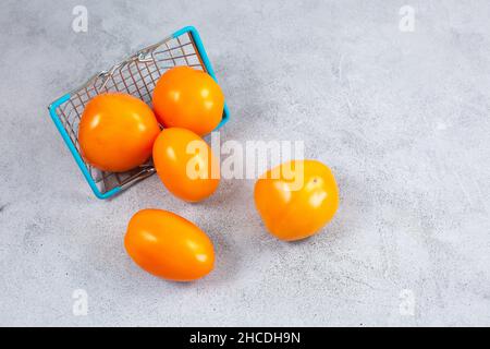 Verstreute gelbe Kirschtomaten in einem Korb auf einem grauen Steingrund. Draufsicht flach liegend. Speicherplatz kopieren Stockfoto