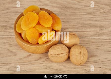 Eine Schüssel getrocknete Aprikosen und drei Walnüsse auf einem Holzgrund Stockfoto