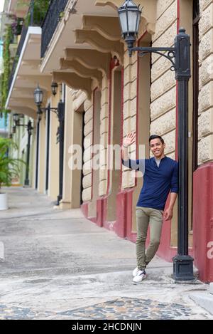 Ein Porträt eines stilvollen jungen Mannes, der lächelnd auf einer Straße in der Stadt winkt. Stockfoto