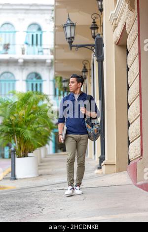 Junger Latino-Mann, der mit seinem Laptop die Straße entlang geht, Panama City, Mittelamerika Stockfoto