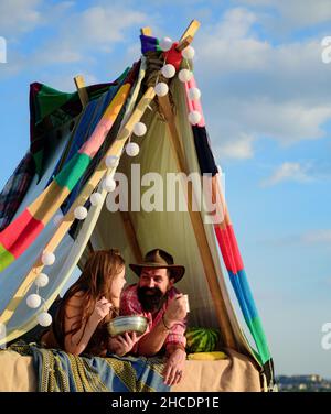 Liebende junge Coupl essen in der Nähe des Zeltlagers. Camping-Paar in der Liebe. Paare von Liebhabern Touristen entspannen sich in der Natur. Campingausflug mit Verliebten. Frühstück inklusive Stockfoto