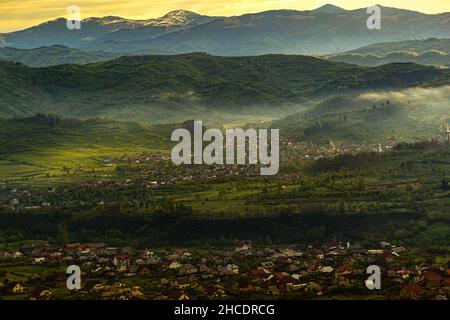 Maramures County mit Häusern aus der Stadt Ieud und den mächtigen Karpaten dahinter, während eines nebligen Sonnenaufgangs. Das Foto wurde am 16th. Mai 2021 in der Nähe von I aufgenommen Stockfoto
