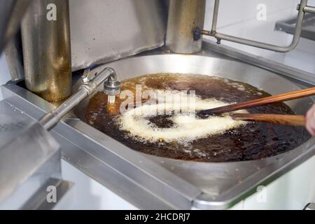 Von oben der rohe Teig für Churros oder porras, der in Öl in einer großen Edelstahlpfanne mit Holzstäben in der professionellen Küche gebraten wird. Typisch spanisches Frühstück Stockfoto