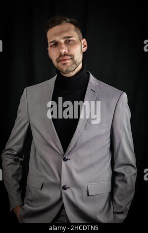 Porträt eines jungen Geschäftsmannes in grauem Anzug und schwarzem Rollkragen, der mit den Händen in den Taschen ernst aussieht Stockfoto