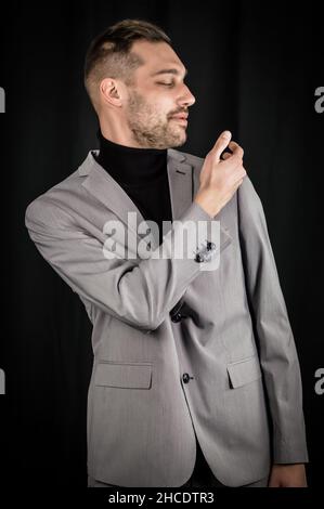Porträt eines jungen Geschäftsmannes in einem grauen Anzug, der sich mit der Hand die Schulter wischt Stockfoto