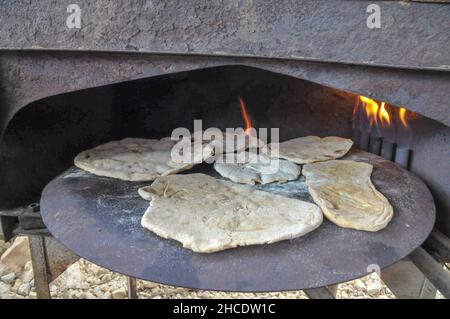 Outdoor Cooking Zubereitung eine flache Brot Pita auf einem saj - eine eiserne Kuppel geformt Pan, das verwendet wird, um das pita Brot auf zu kochen. Es ist mehr als eine Quelle von h platziert Stockfoto