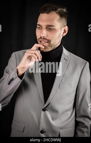 Porträt eines jungen Geschäftsmannes in einem grauen Anzug, der sein Kinn mit den Fingern hält und zu zögern scheint, während er nachdenkt Stockfoto