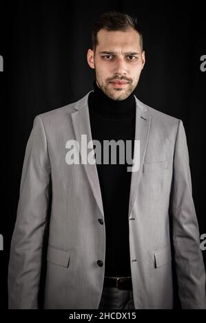 Porträt eines jungen Geschäftsmannes in grauem Anzug und schwarzem Rollkragen, ernst aussehend, Nahaufnahme Stockfoto