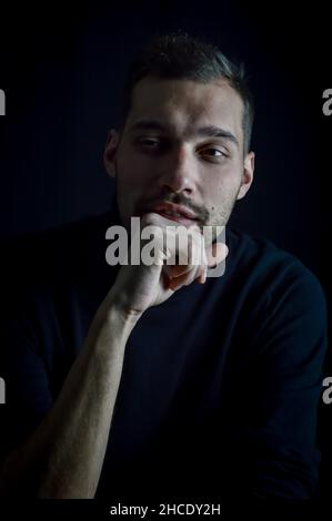 Porträt eines jungen Mannes, dessen Hand auf seinem Kinn liegt und der nachdenklich wegschaut Stockfoto