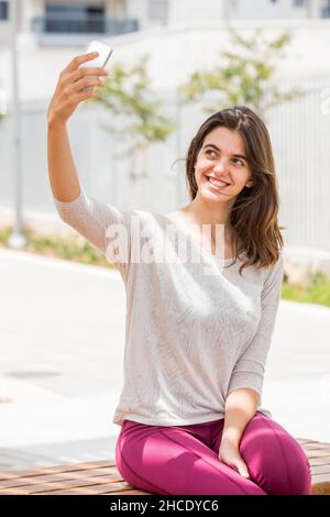 Junge Frau in legerer Sportkleidung nimmt ein Selfie draußen Stockfoto