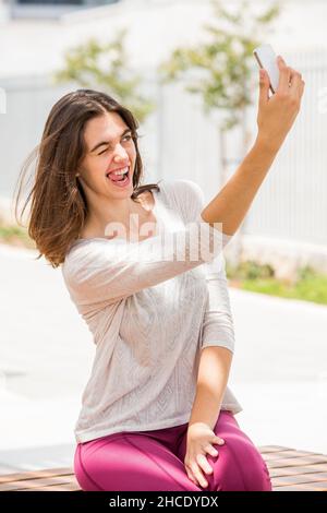 Eine junge Frau in legerer Sportkleidung macht ein Selfie, während sie ihr Gesicht zieht Stockfoto