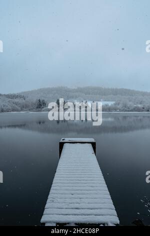 Hölzerner Pier auf See mit frischem Schnee bedeckt.Winterteich mit kleinem Steg am nebligen Morgen.Foggy bewölkte Landschaft im Wasser reflektiert. Weißer Winter Stockfoto