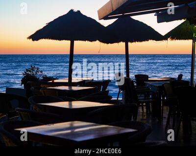 Tische und Sonnenschirme eines Restaurants mit Blick auf den Strand von Almuñecar in Granada bei Sonnenuntergang. Stockfoto