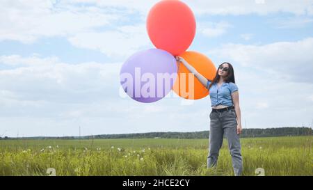 Glückliches Mädchen mit großen bunten Ballons posiert auf dem Feld. Stockfoto