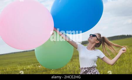 Glückliches Mädchen mit großen bunten Ballons posiert auf dem Feld. Stockfoto