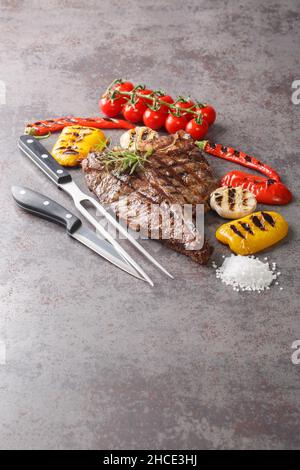 Saftiges, großes T-Bone-Steak auf dem Grill serviert mit gegrilltem Gemüse aus der Nähe auf einem betongrauen Hintergrund. Vertikal Stockfoto