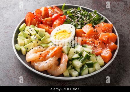 Keto Diätportion zum Frühstück mit Lachs, Garnelen, Eiern und frischem Gemüse in Nahaufnahme auf einem Teller auf einem Betontisch. Horizontal Stockfoto